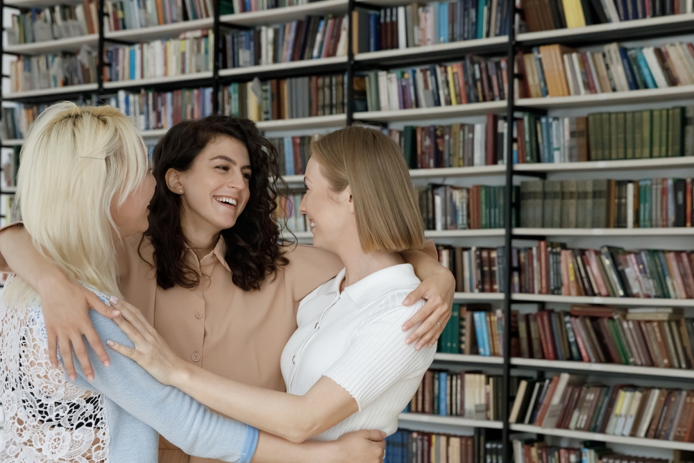 Three,Students,Girls,,Best,Friends,Meets,In,Library,Hugging,Glad