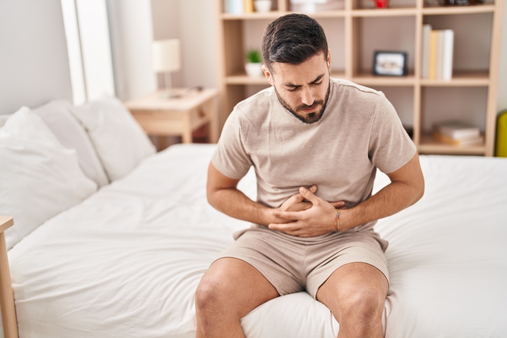 Young,Hispanic,Man,Suffering,For,Stomachache,Sitting,On,Bed,At