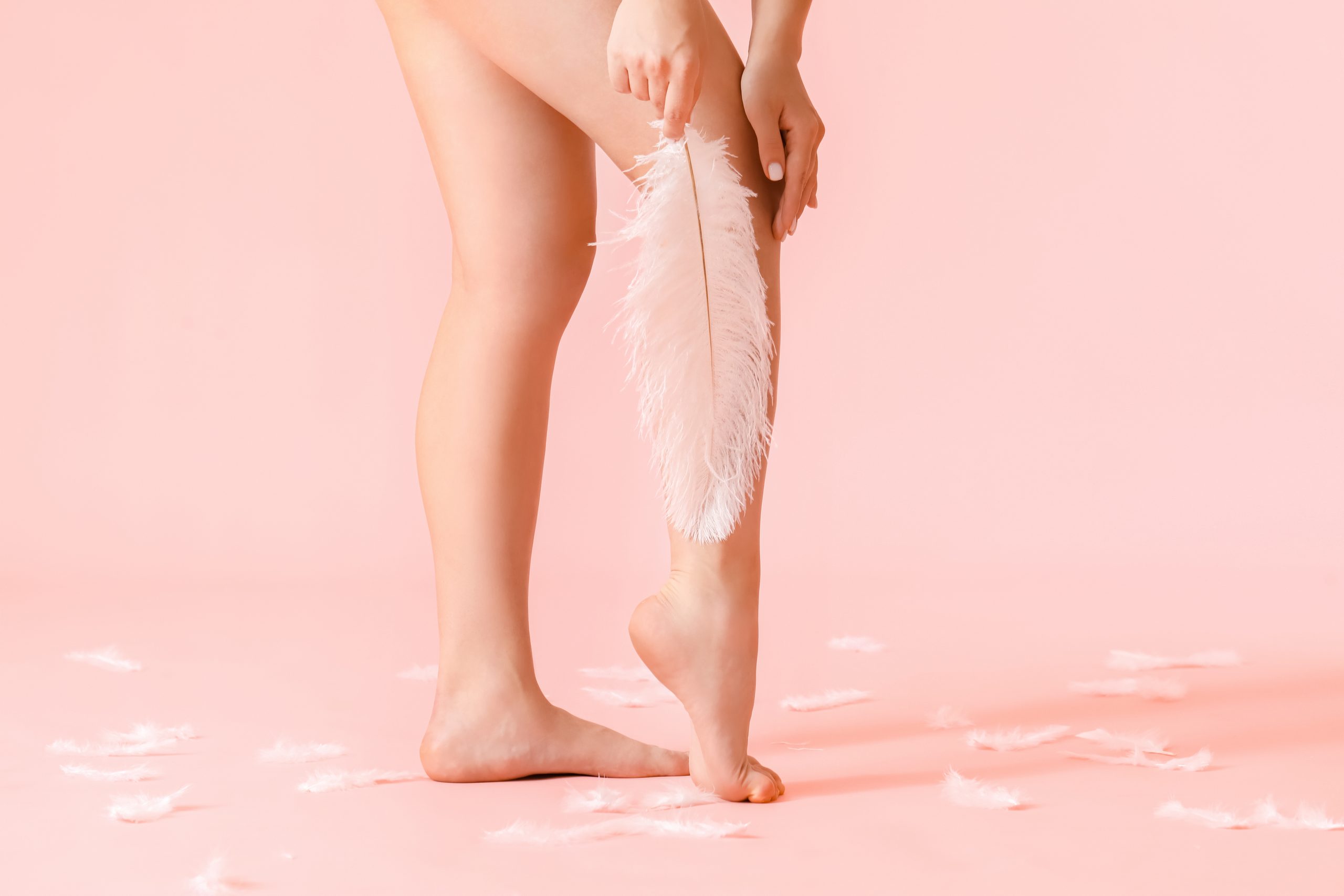 Beine von jungen Frauen mit weicher Feder auf Farbhintergrund. Epilation-Konzept