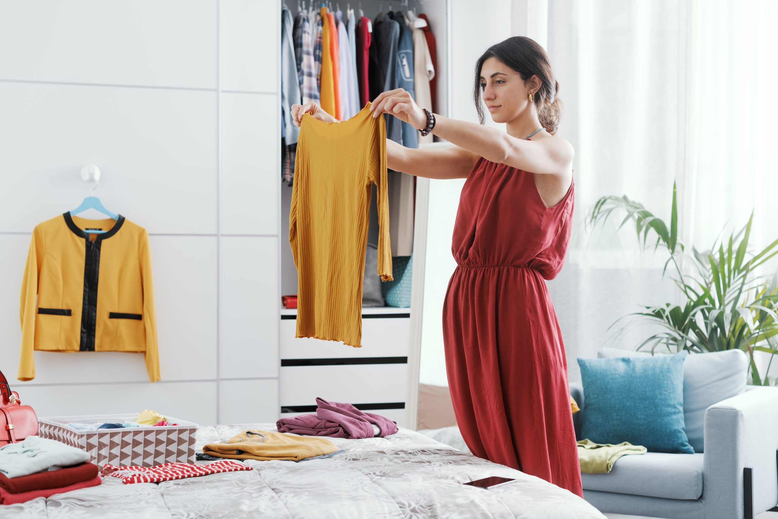 Elegante Frau in ihrem Schlafzimmer, sie enttäuscht ihren Kleiderschrank und wählt Kleidung aus