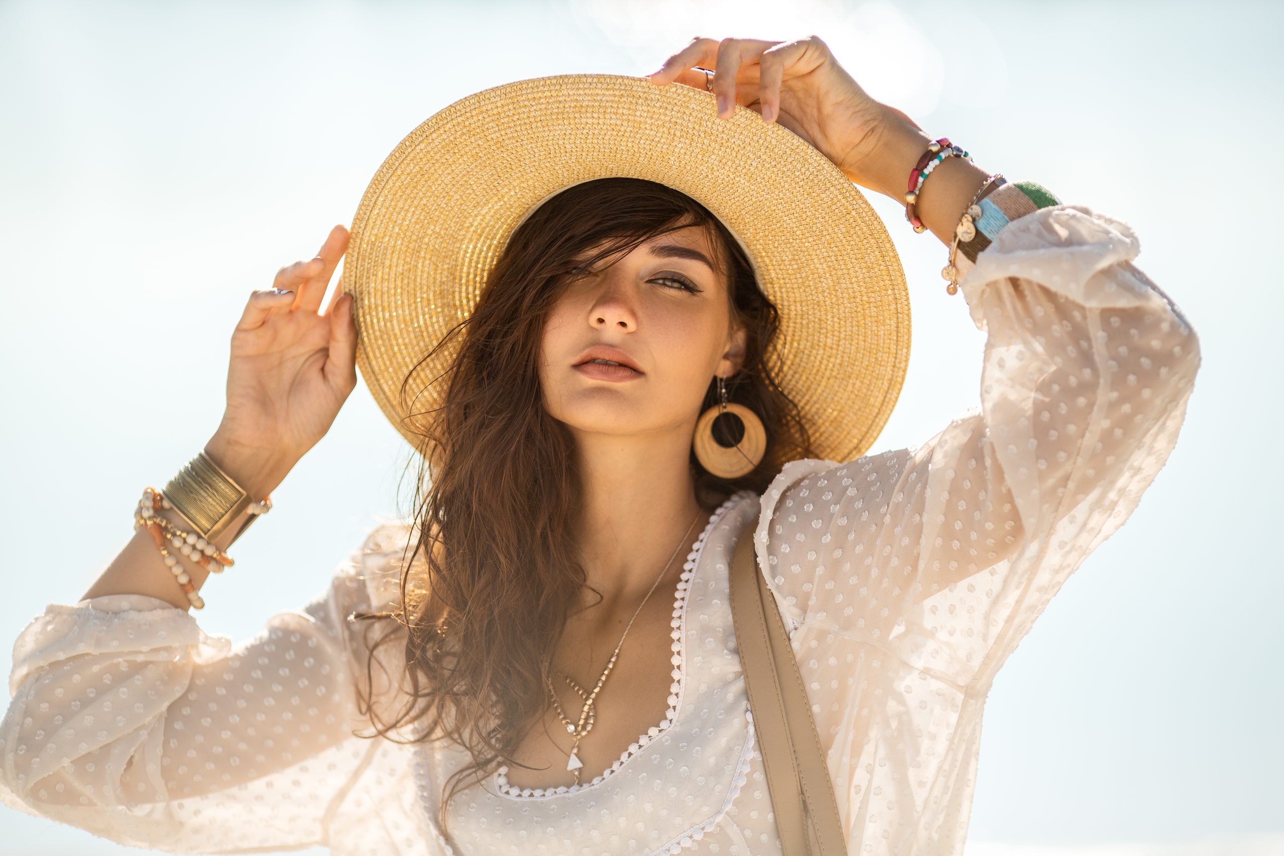 Outdoor-Modeporträt von romantischer Dame, die auf einem Strand auf einem schönen Bokeh-Hintergrund steht. Tanned Mädchen in modischem schicken Boho-Stil, die Kamera anschauen. Reisen, Sommerurlaub