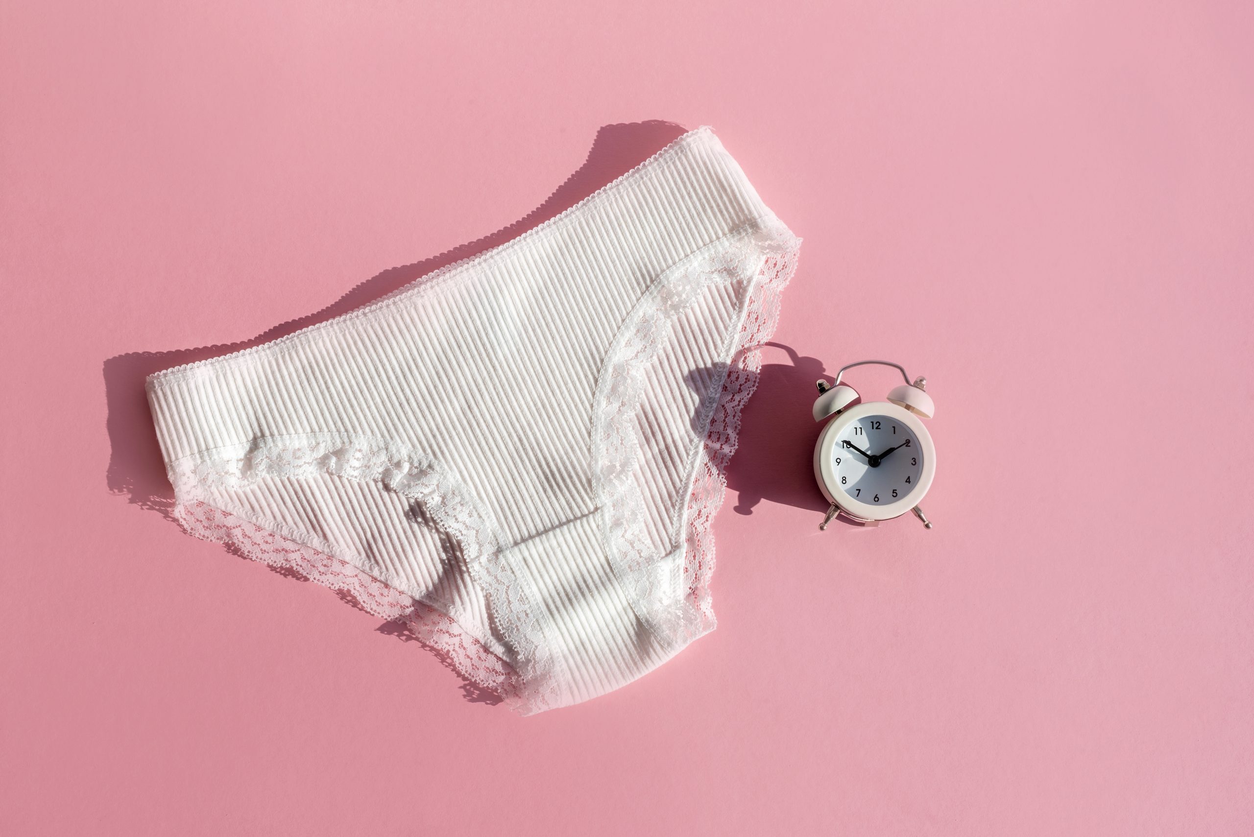 Frauen Unterwäsche und Wecker. Konzept der Wechseljahre, kritische Tage, Bauchschmerzen, Menstruation, Menstruationszyklus, Gesundheit der Frauen. Gynäkologie, weibliche Erkrankungen, hormonelles, prämenstruelles Syndrom