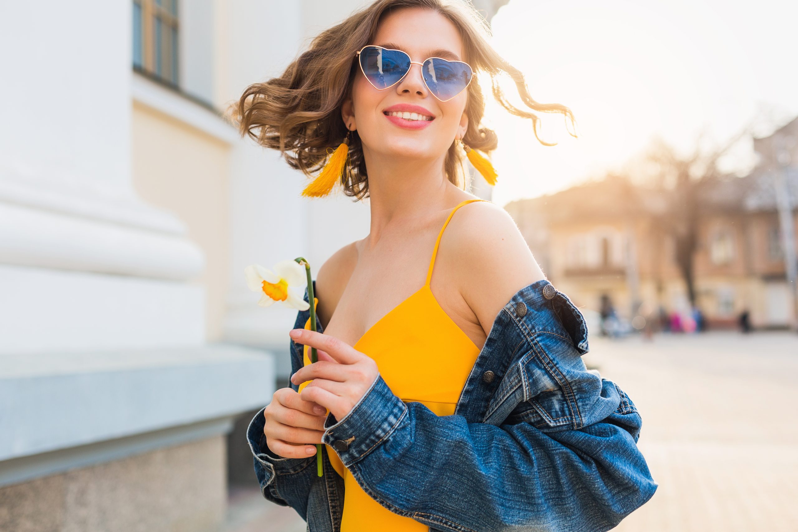 schöne Frau winkend Haare lächeln, stilvolles Kleid, mit Jeansjacke und gelbem Oberteil, Mode, Sommerstil, fröhliche positive Stimmung, sonniger Tag, Sonnenaufgang, Straßenmode, blaue Sonnenbrillen