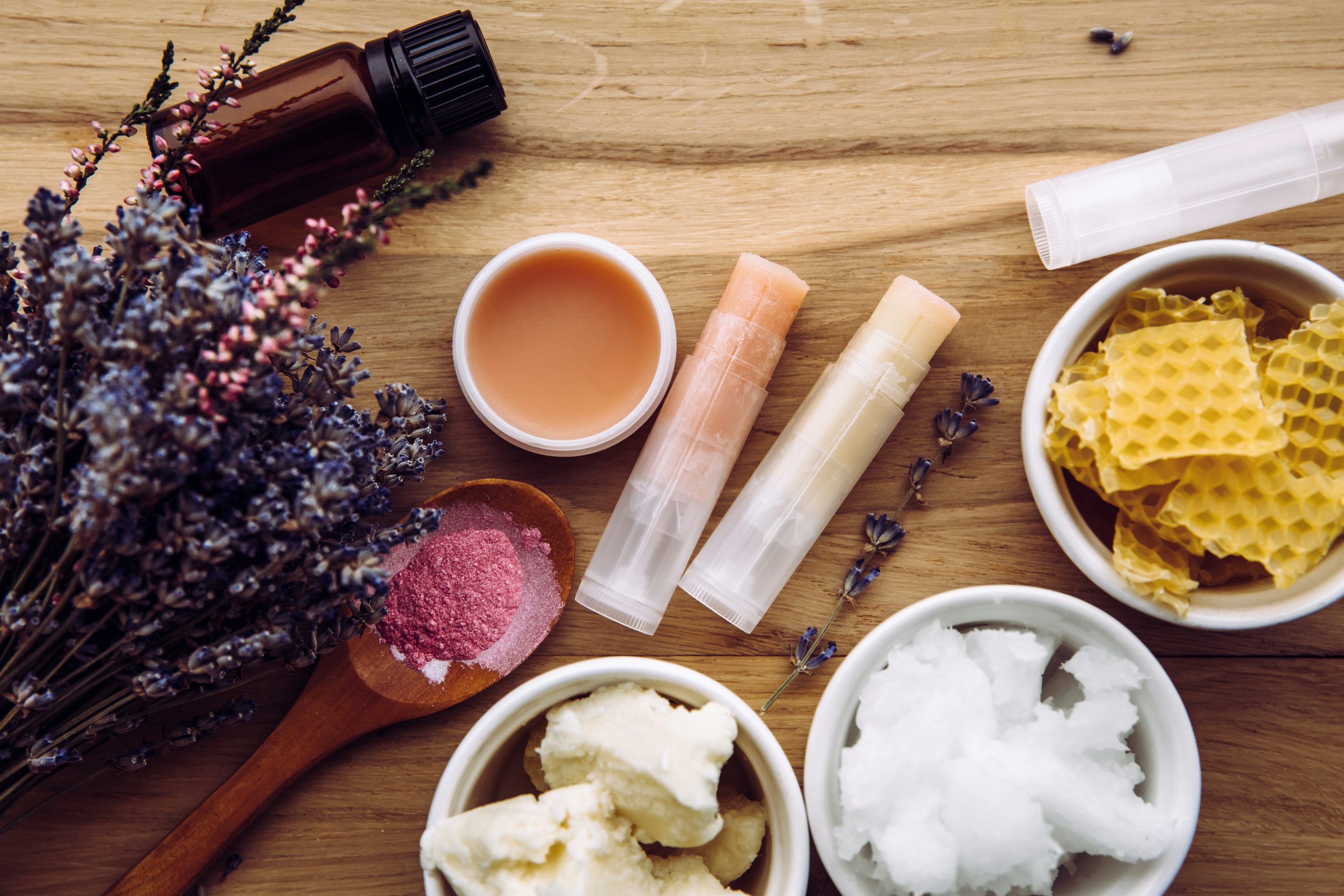 Bestandteile für hausgemachte Lippenbalsam: Schaffleisch, ätherisches Öl, mineralisches Farbpulver, Bienenwachs, Kokosöl. Hausgemachte Lippenbalsam-Lippenstift-Mischung mit herumstreuten Zutaten.