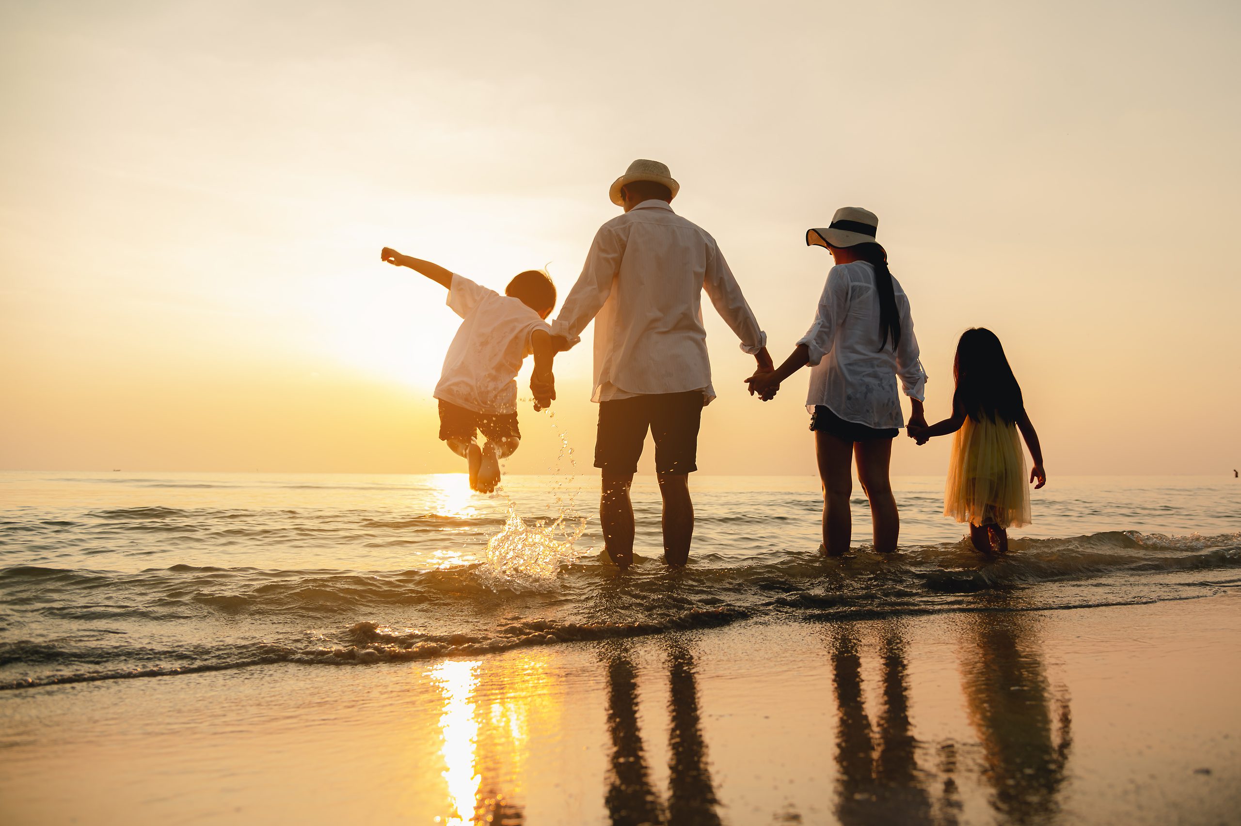 Fröhliche asiatische Familie springt im Urlaub am Strand zusammen. Silhouette der Familie, die Hände genießt den Sonnenuntergang am Strand.Glückliche Familie und Urlaub Konzept.