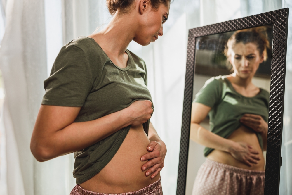 Frown,Young,Woman,Standing,In,Front,Of,A,Mirror,And