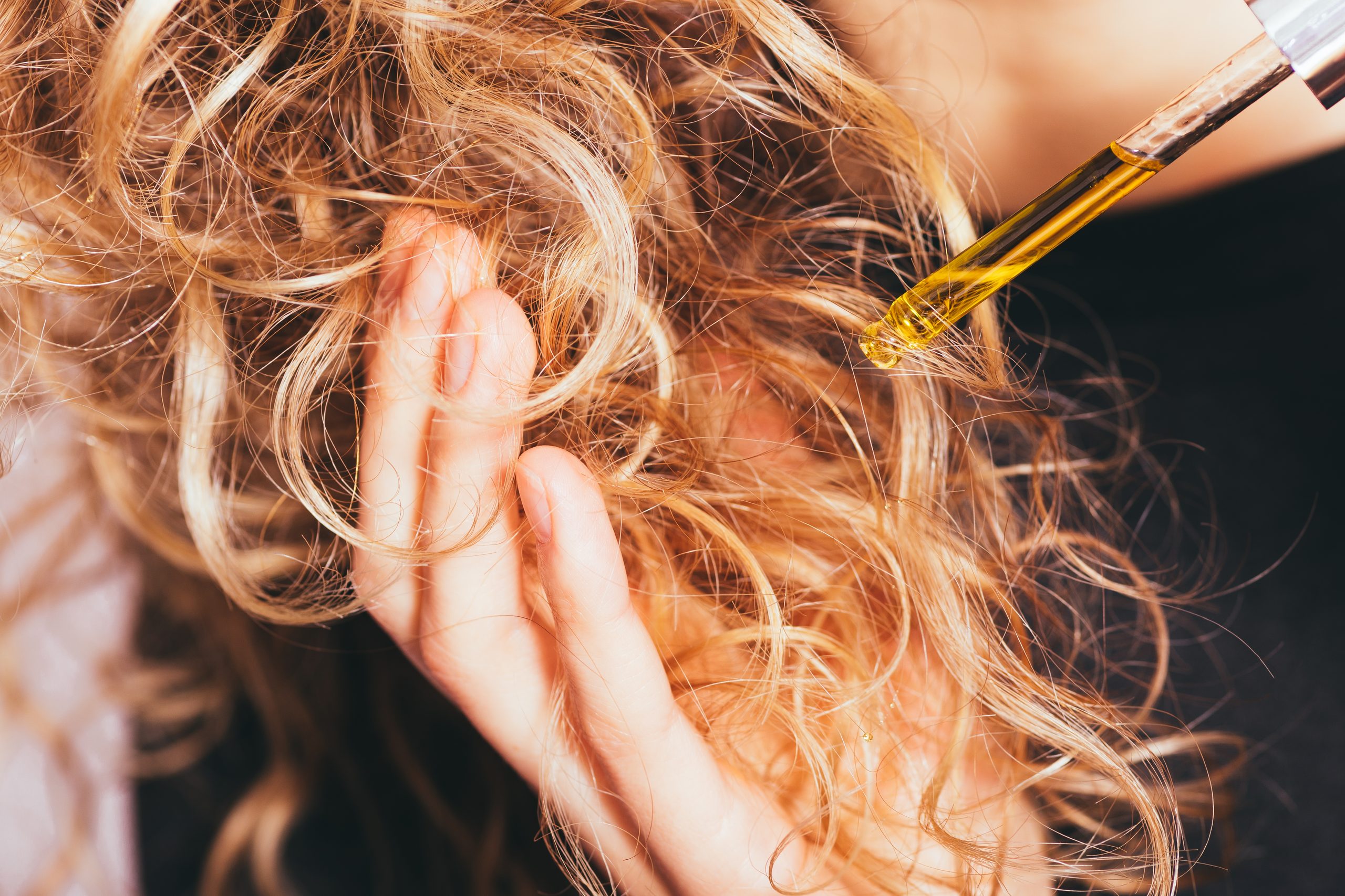 Nahaufnahme einer jungen Frau, die Pipettenöl auf ihr lockeres Haar aufträgt