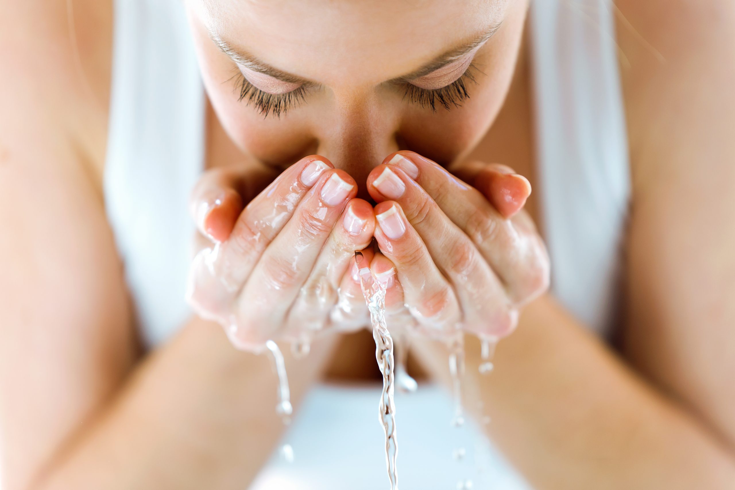 Porträt einer schönen jungen Frau, die ihr Gesicht waschen und Wasser in einem häuslichen Badezimmer spritzen.