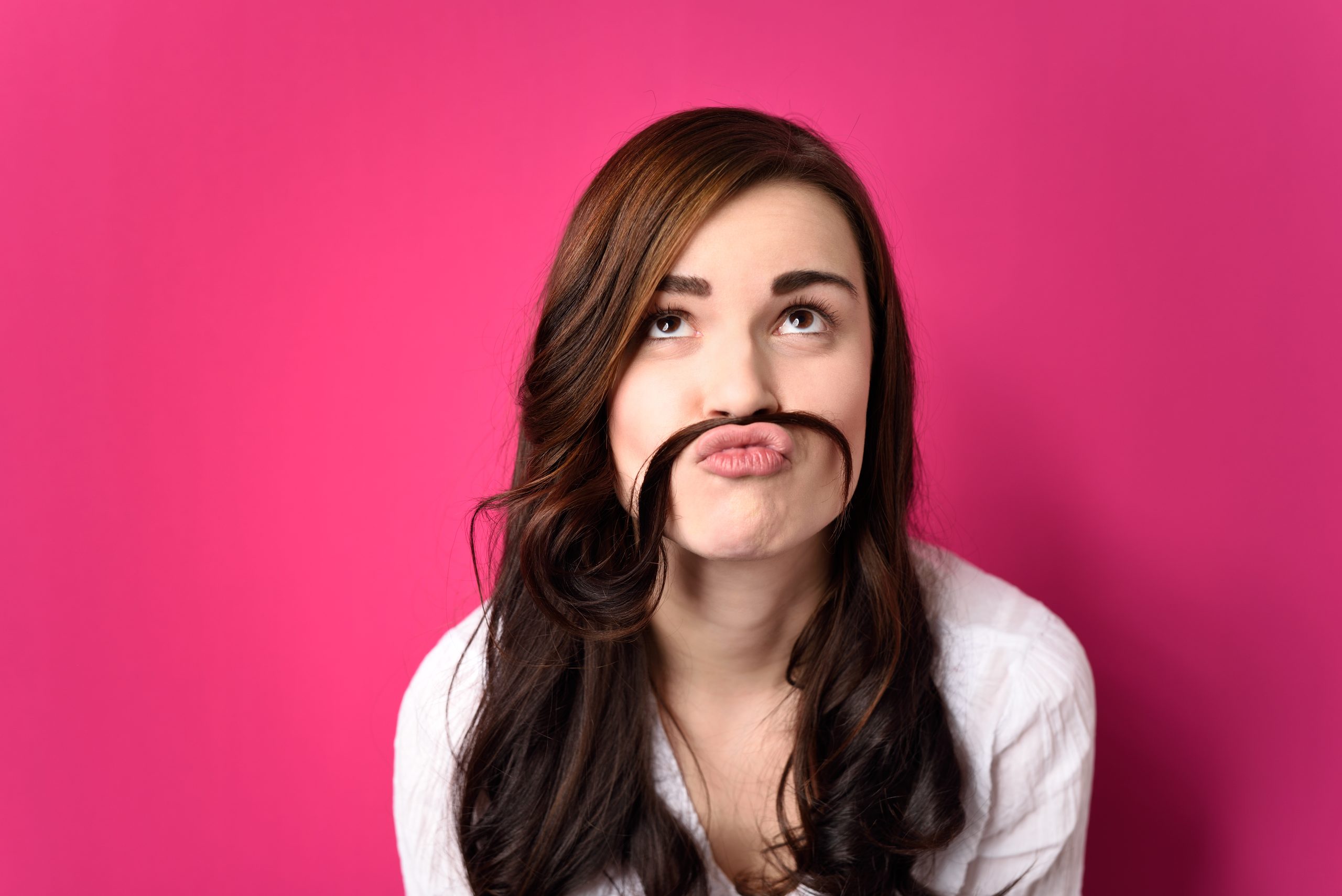 Nahaufnahme Funny Young Woman Putting ihre Haare zwischen Nase und Lip und Blick nach oben. Einzeln auf rosafarbenem Hintergrund.