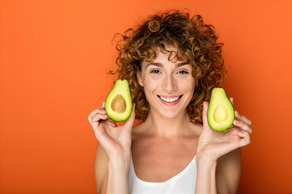 Young,Curly,Woman,Holding,A,Avocado,In,Hands,On,Orange