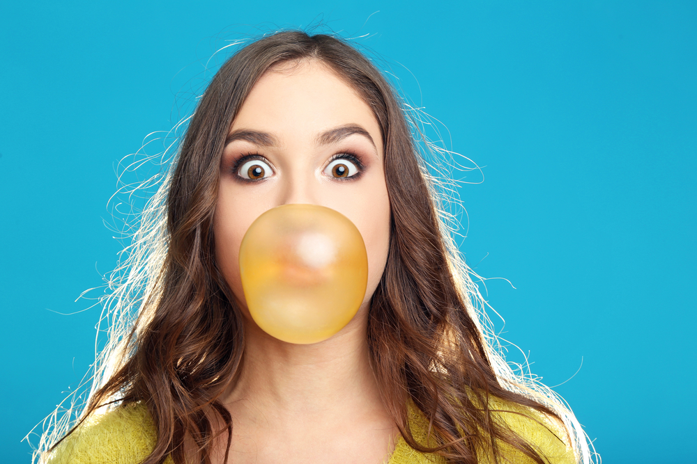 Beautiful,Young,Girl,Blowing,Bubble,With,Chewing,Gum,On,Blue