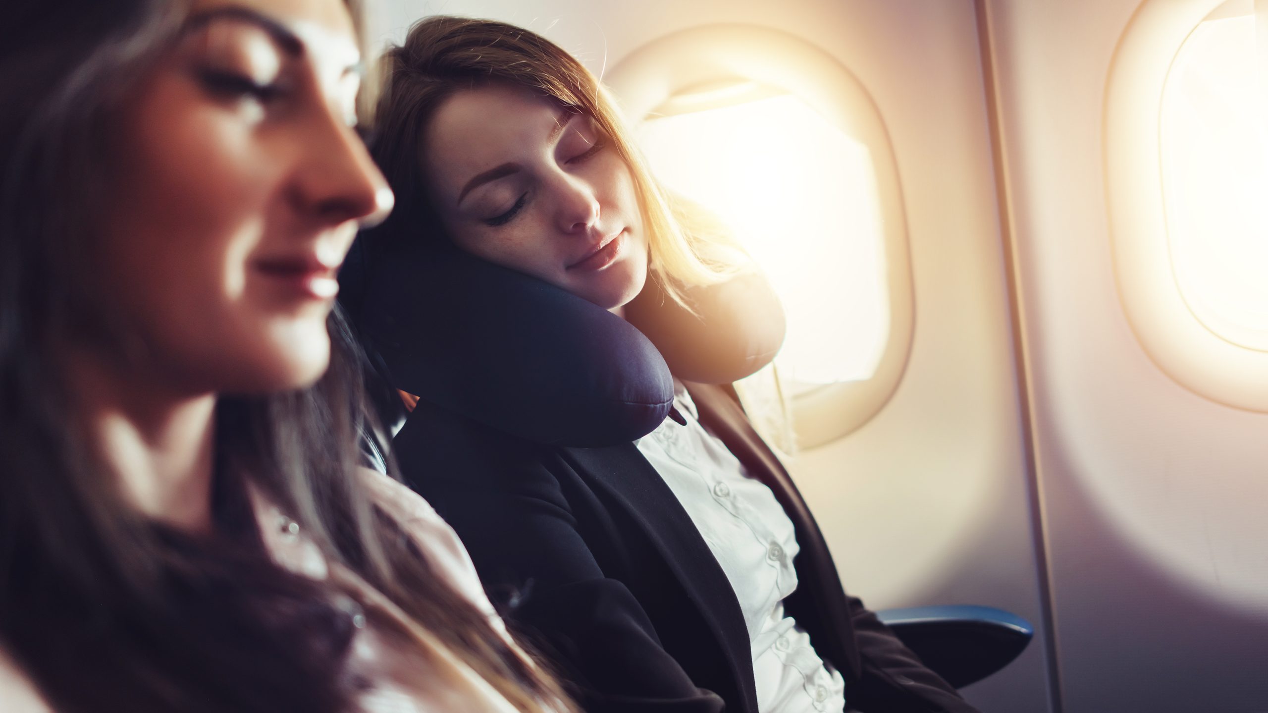 Freundinnen, die mit dem Flugzeug reisen. Eine Fluggastin, die im Flugzeug auf Nackenkissen schläft.
