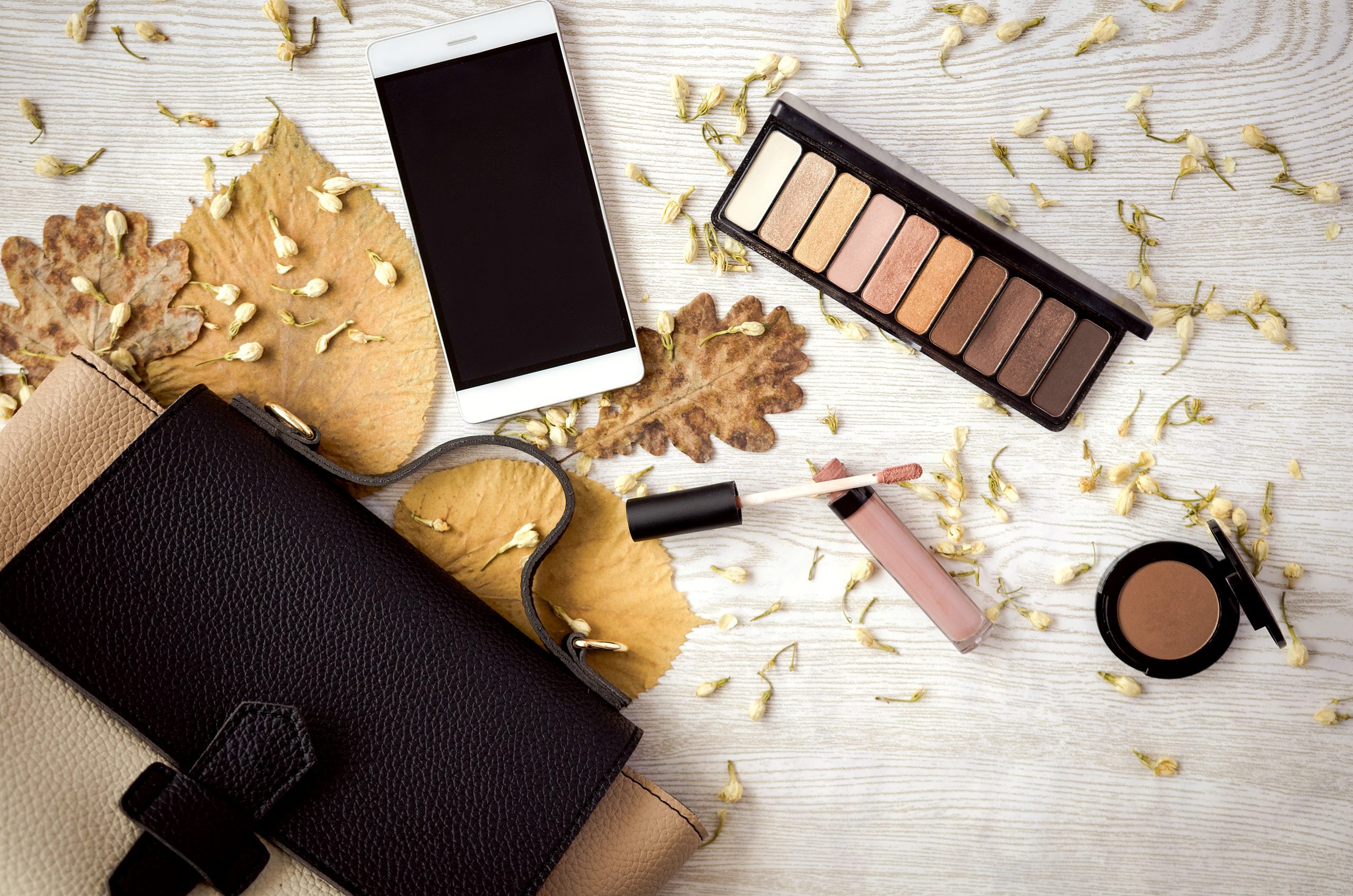 Make-up Zeug, Handy und weibliche Tasche auf weißem Tisch mit Blättern. Herbstzeit.