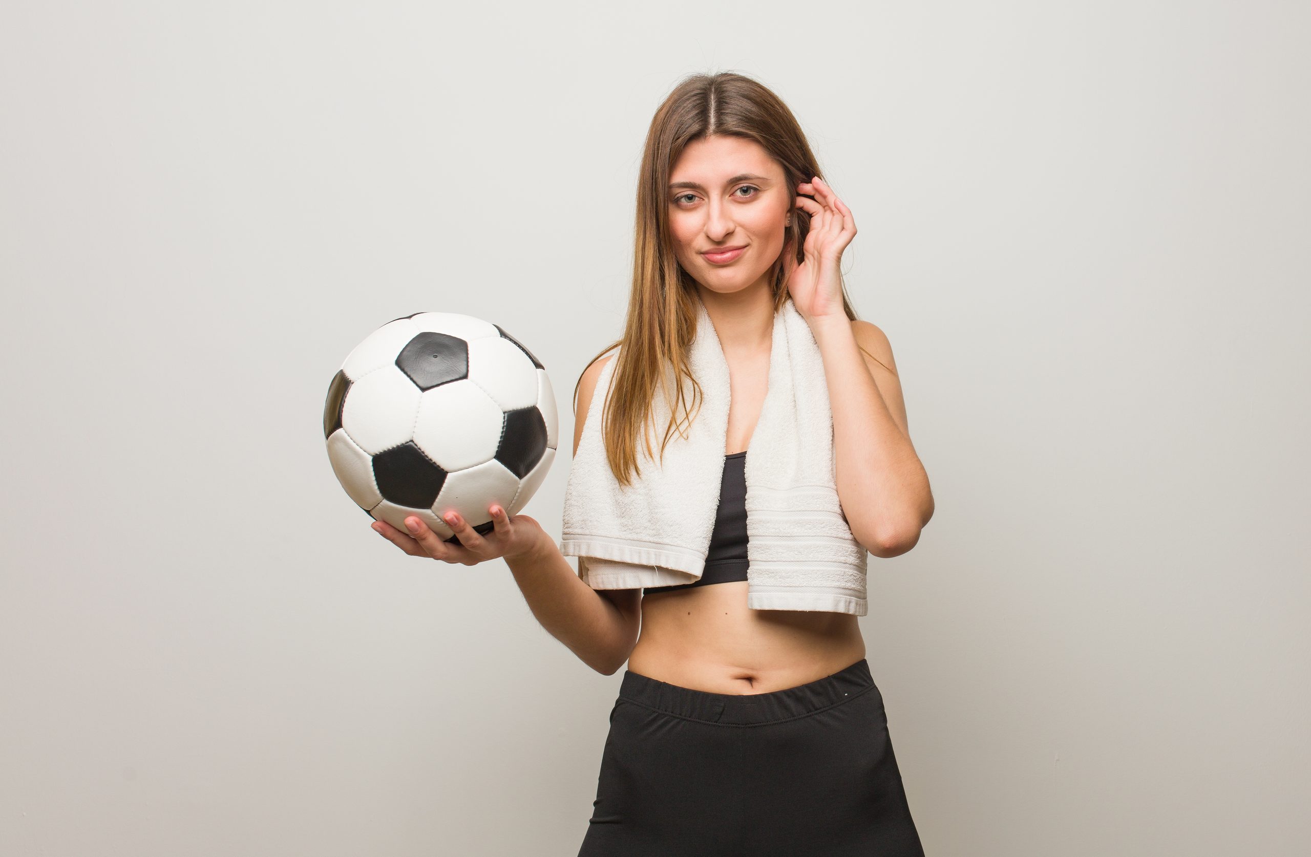 Young fitness russian woman covering ears with hands. Holding a soccer ball.