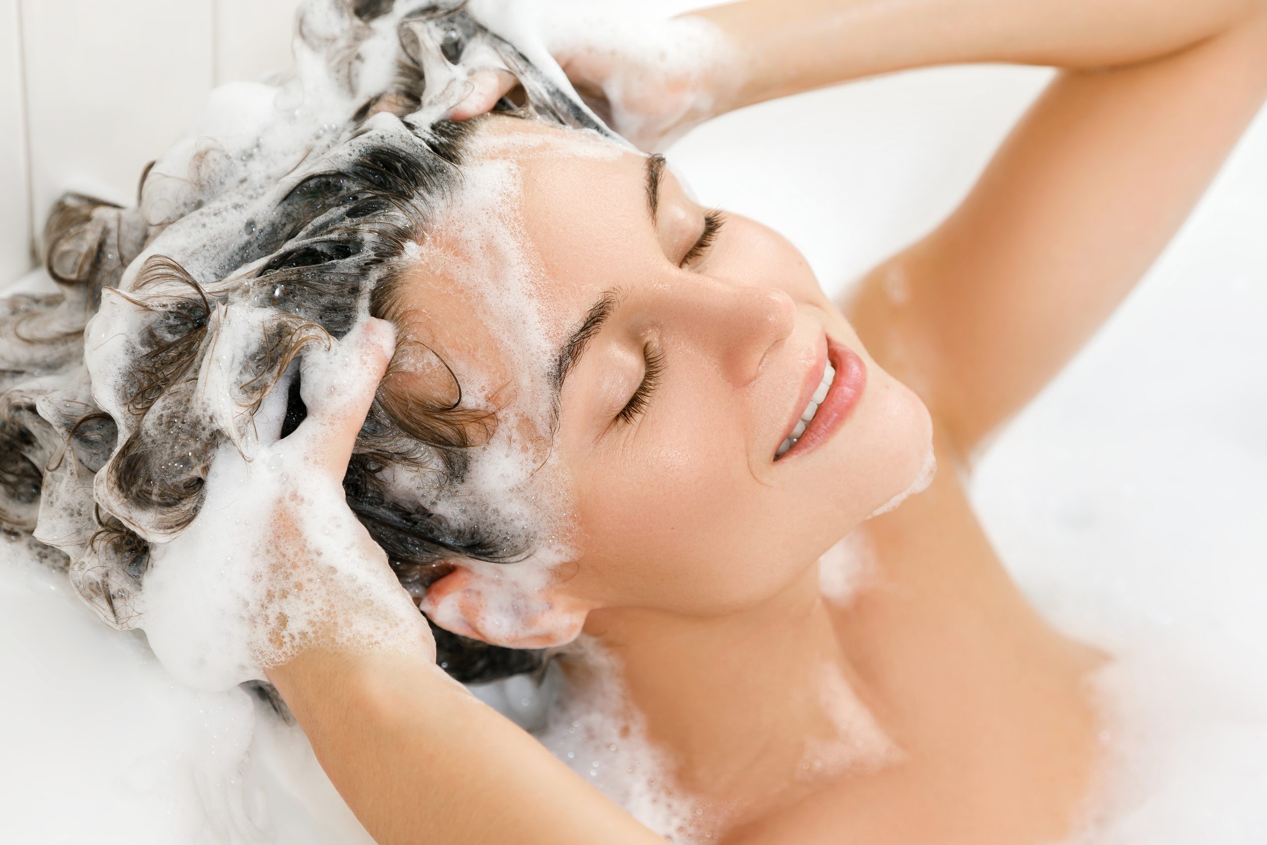 Junge und schöne Frau wäscht sich das Haar mit Shampoo
