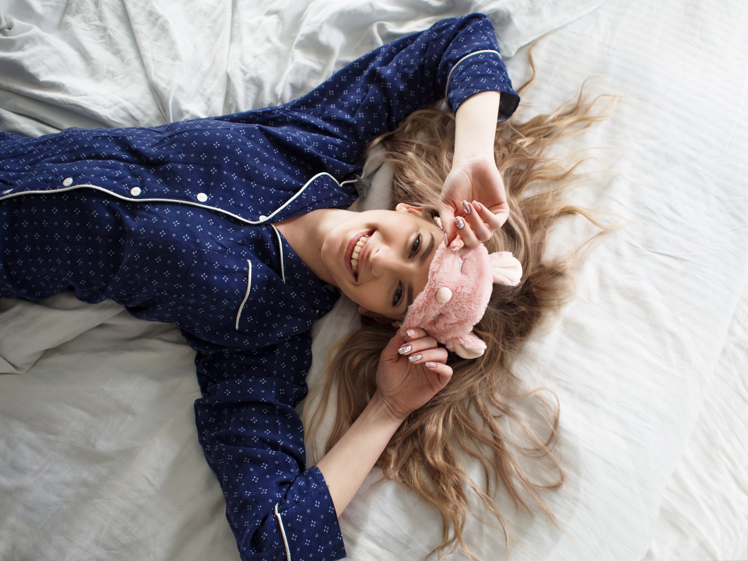 Feine Blondine im Bett in blauen Schlafanzügen und Schlafmaske, Draufsicht