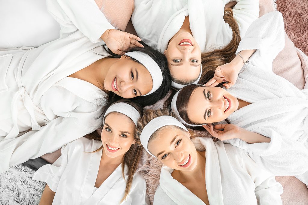 Happy young women lying on bed during hen party, top view