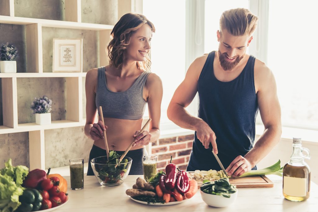 Schöne junge Sportler sprechen und lächeln, während sie zu Hause gesund kochen in der Küche