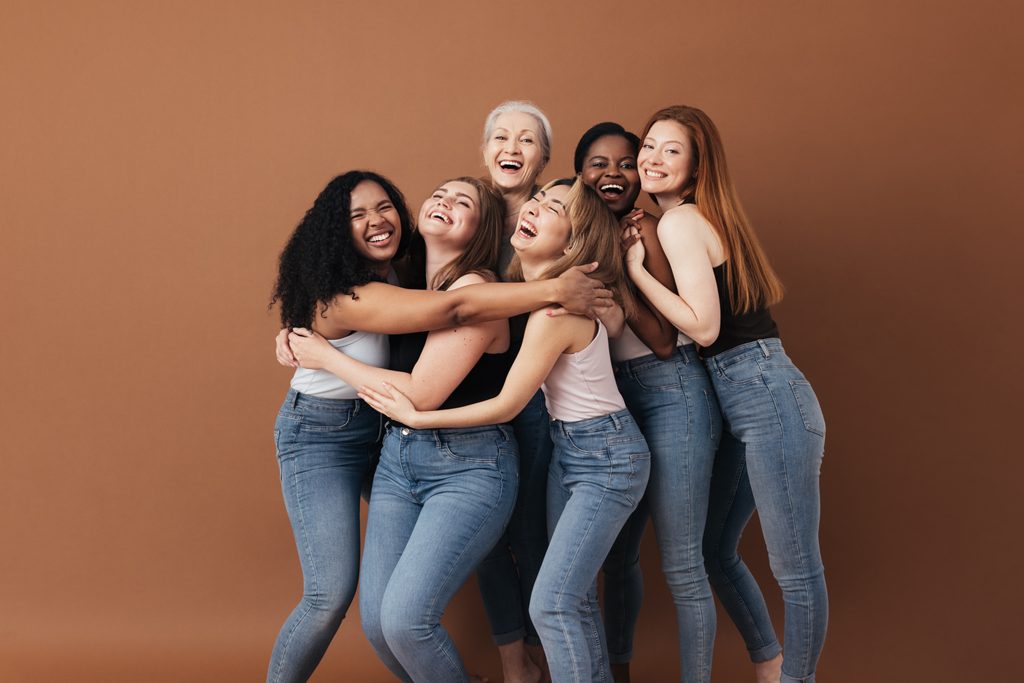 Sechs lachende Frauen einer anderen Rasse, eines anderen Alters und einer anderen Figur. Gruppe multiethnischer Frauen, die sich auf braunem Hintergrund amüsieren.