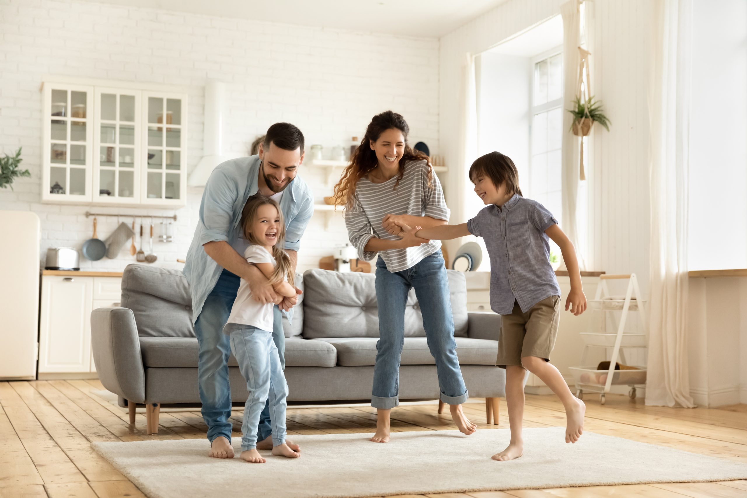 Fröhliche Familie, die ein lustiges Spiel spielt, das zusammen mit dem kleinen Sohn und der Tochter im modernen Wohnzimmer Spaß hat. Junge Papa und Mutter mit süßen und süßen Kindern, die Sport treiben, das Wochenende zu Hause genießen.