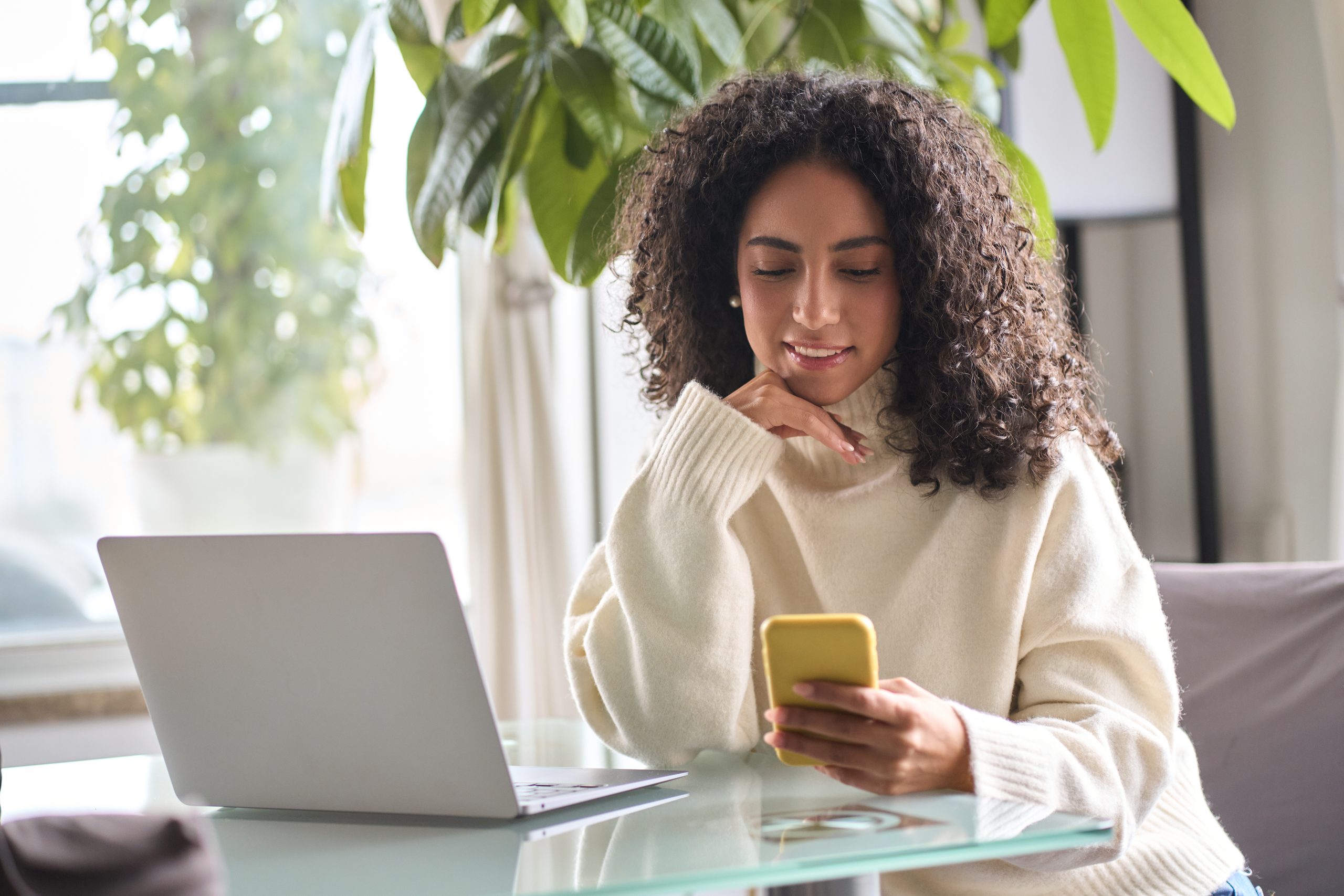 Junge Frau benutzt ein Smartphone und einen Laptop.