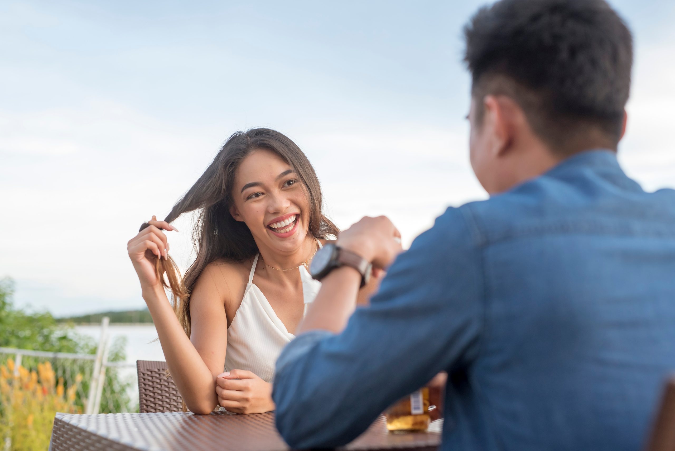 Eine junge Frau wirbelt sich die Haare, während sie ihr Date aufmerksam zuhört. Interessiert und angezogen für einen Mann, den sie mag. Ein erstes Date geht gut. Café-Szene im Freien.