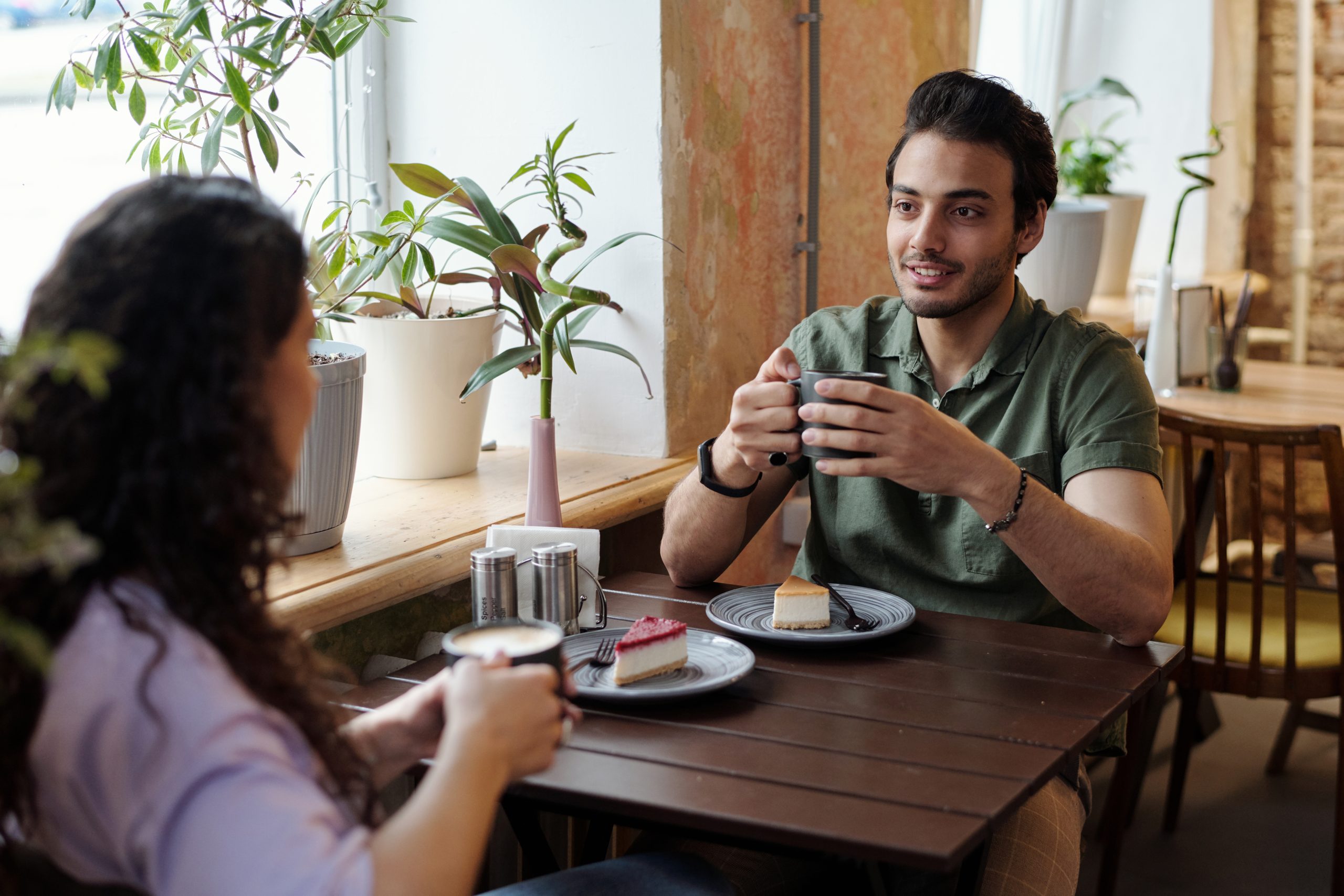 Guy mit einer Tasse Kaffee und seiner Freundin sitzt am Tisch vor dem anderen und chattet beim Kaffee mit leckerem Nachtisch